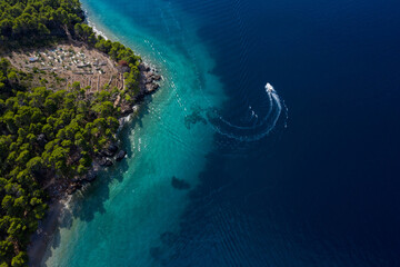 Tourist boat on the emerald sea from a bird's eye view, beautiful coastline covered with thick trees. Makarska riviera in Dalmatia, Croatia