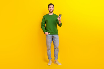 Fototapeta na wymiar Full body photo of handsome young blogger wear green jumper new jeans search phone booking hotel isolated on yellow color background