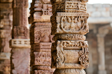 Stone columns with decorative bas relief of Qutb complex in South Delhi, India, close up pillars in ancient ruins of mosque landmark, popular touristic spot in New Delhi, ancient indian architecture