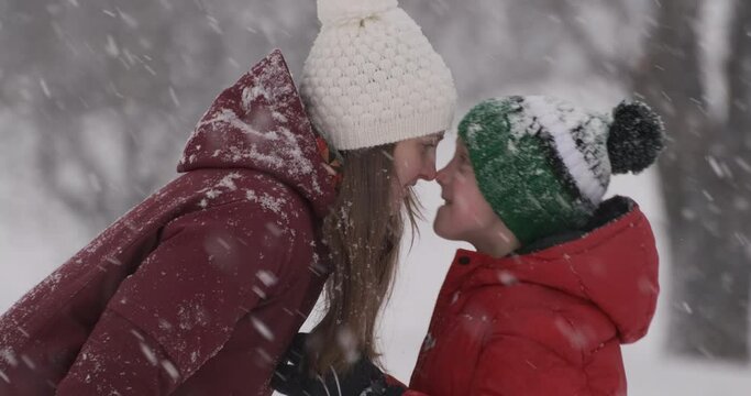 Mom and son touch with their noses and fool around in the winter forest. Mother and her child enjoying beautiful cold winter day.