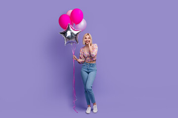 Full body portrait of astonished cheerful lady hand touch cheek hold air balloons empty space isolated on purple color background