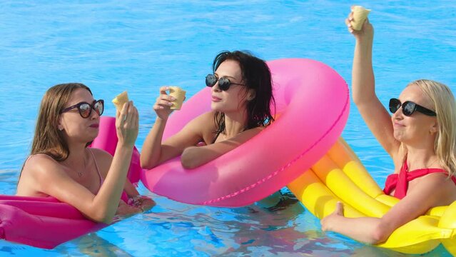 Beautiful young women swim in the pool on inflatable rings and eat ice cream. Close-up of happy people on vacation, at a party.
