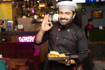 Waiter holding plates with food and giving happy expression at restaurant