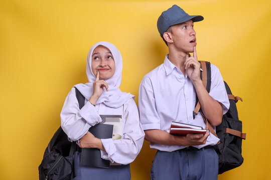 Two happy Indonesian high school  students in white and grey uniform thingking and smiling at copy space