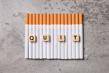 Cigarettes arranged in a row with word Quit on gray rustic background. Stop smoking, no tobacco day concept.
