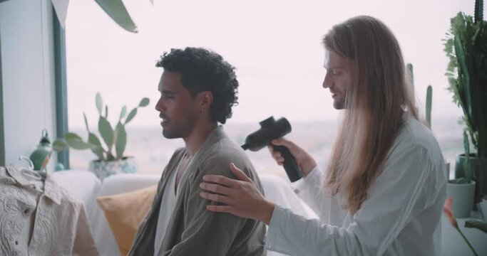 Young queer man giving a massage to his partner with a massage gun. 