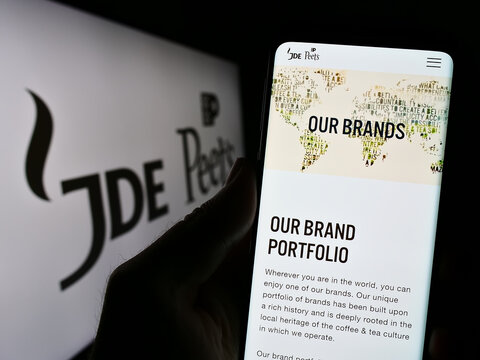 Stuttgart, Germany - 08-05-2023: Person holding cellphone with website of beverage company JDE Peet's N.V. on screen in front of business logo. Focus on center of phone display.