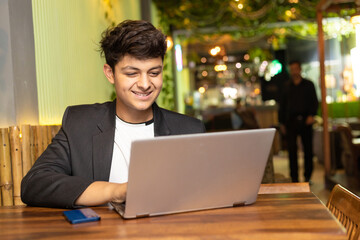 Young indian boy giving happy expression after looking in laptop at restaurant