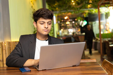 Young indian boy using laptop at restaurant