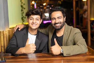 Indian father and son showing thumps up at restaurant