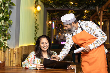 Indian women select dishes in menu card and giving food order to waiter at restaurant
