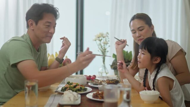 asian happy family spend time have breakfast or dinner on table together at sunlight.Little kid daughter enjoy eat yummy food with father,asian mother.asia family day meet talk at home