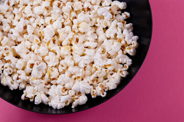 Popcorn in the black bowl on a pink background.