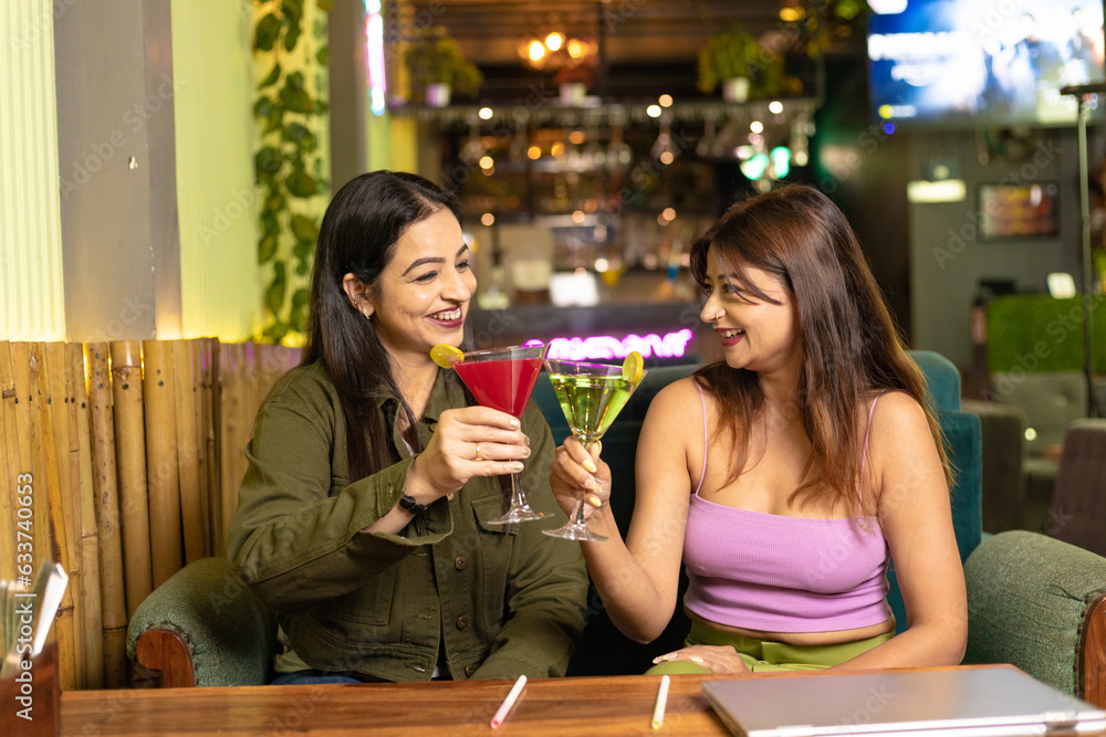 Wall mural Two indian female friends enjoying cold drinks together at restaurant