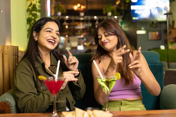 Two indian female friends discussing, laughing and enjoying party together at restaurant.