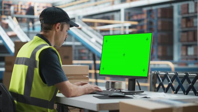 Caucasian Male Stocking Associate Using Green Screen Chromakey Desktop Computer In Modern Distribution Facility. Diverse Employees Working With Online Orders, Loading Cardboard Boxes On Conveyor Belt.