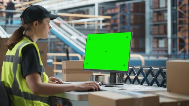 Caucasian Female Stocking Associate Using Desktop Computer To Check Inventory In Distribution Facility. Diverse Employees Working With Online Orders, Loading Cardboard Boxes On Conveyor Belt.