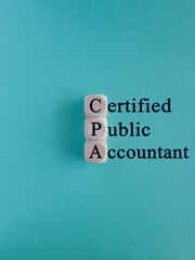Wooden cubes building word CPA - abbreviation of certified public accountant on light blue background. Business concept. Copy space.