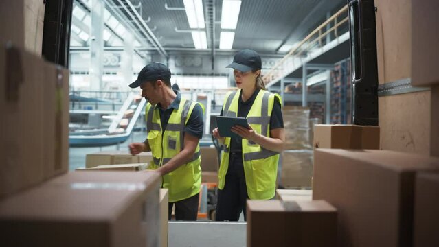 Caucasian Female Supervisor Using Tablet Computer To Check Inventory In Modern Logistics Facility With Conveyor Belt. Male Warehouse Worker Loading Boxes In Van For Delivering Orders To Clients.