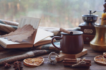 Autumn mood, autumn atmosphere. A cup of hot coffee, a plaid blanket, a coffee mill, cinnamon sticks, star anise, a book on a wooden windowsill on a rainy day.