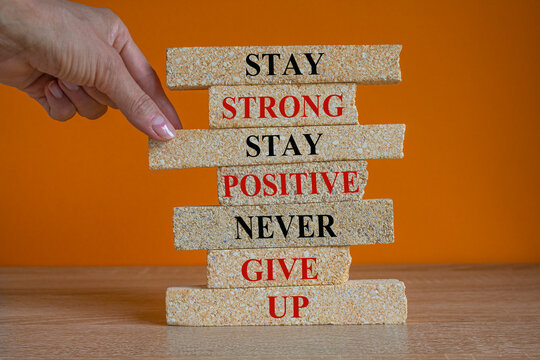 Brick blocks with concept red words Stay strong stay positive never give up. Beautiful orange background. Copy space. Businessman hand. Motivational business never give up concept.