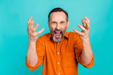 Photo of shocked angry man dressed orange shirt screaming rising hands arms isolated turquoise...