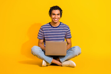 Full size portrait of cheerful nice person sit floor crossed legs use netbook networking isolated on yellow color background