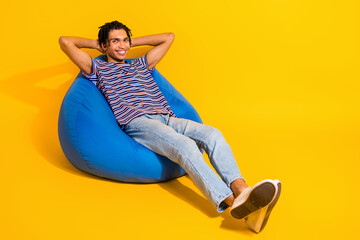 Full body photo of satisfied young man sit comfy bag hands behind head isolated on bright yellow...