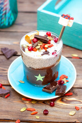 Chia pudding with chocolate, fresh cranberries, almonds, chopped chocolate bars, pumpkin seeds and goji berries on rustic background