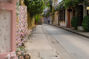 Narrow street of old town in Cartagena city with colorful painted buildings facades, cafes, bars, souvenir stores and blooming flowers. Selective focus.