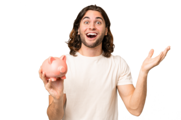 Young handsome man holding a piggybank over isolated background with shocked facial expression