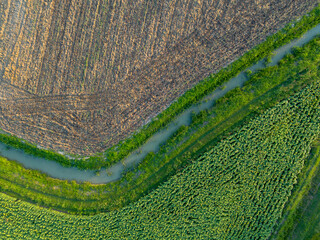 Aerial view of cultivated agricultural farmland divided by a stream with water for watering