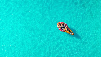 Relaxed girl on an inflatable mattress in the pool in the summer relaxes and swims, shot from above...