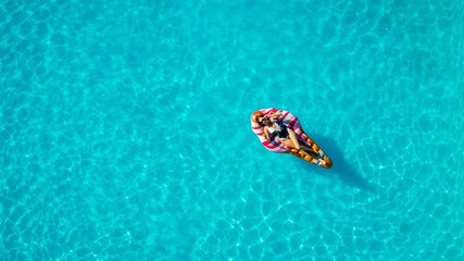 Relaxed girl on an inflatable mattress in the pool in the summer relaxes and swims, shot from above by a drone