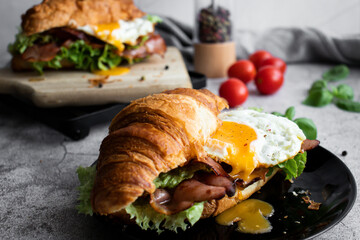 Croissant sandwich with bacon, egg and salad. on wooden board