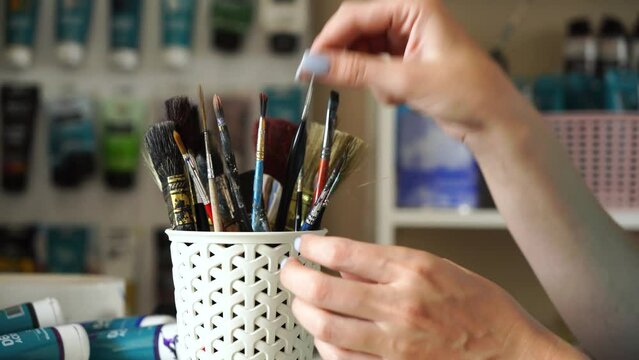 A female artist prepares brushes for painting in her studio.