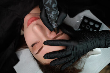The master holds the model's eyebrows with his fingers and applies the eyebrow permanent. Eyebrow...