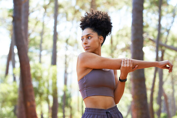 Serious multi-ethnic woman stretches arms before trail run in forest, exercise - Powered by Adobe