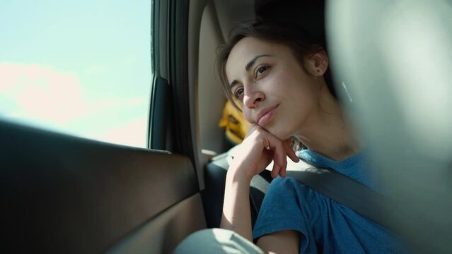 young woman sitting close to window in moving car and looking outside. girl is bored during long road trip in summer in car. summertime vacation car traveling