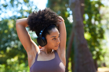 Beautiful multi-ethnic woman stretches arms overhead with headphones, run forest