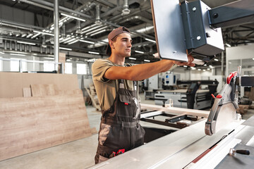 Young carpenter cutting a piece of wood in using a circular saw in furniture factory