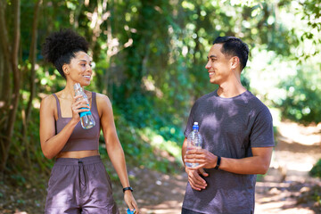 Two tired fitness partners drink water on trail run through forest, exercise