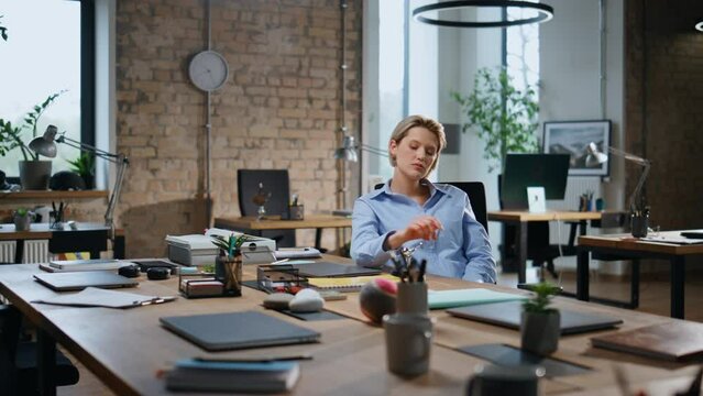Weary woman entrepreneur looking at table pendulum sitting empty office overtime