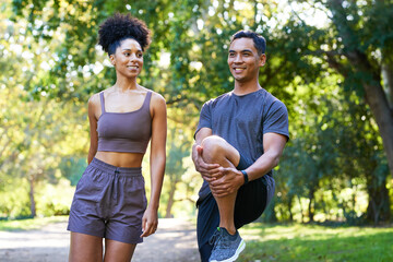 Beautiful couple stretch legs together before running in park, fitness trail run