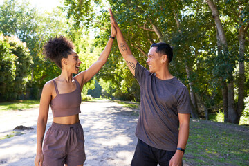 Beautiful young fit couple give high five after exercise in park, trail run