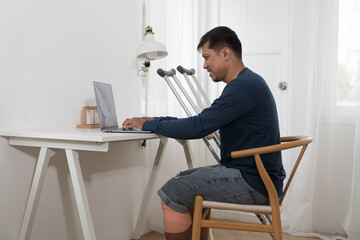 Asian male with crutches sitting and working on table office at home