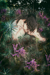 woman nestled among the plants and flowers of a garden