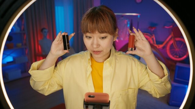 Girl beauty blogger holding two closed boxes of lipsticks and demonstrating them in front of the camera at home