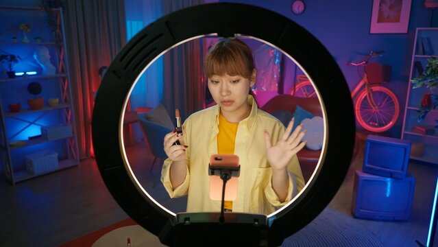 Girl beauty blogger in casual clothing demonstrating a red lipstick in front of the camera at home