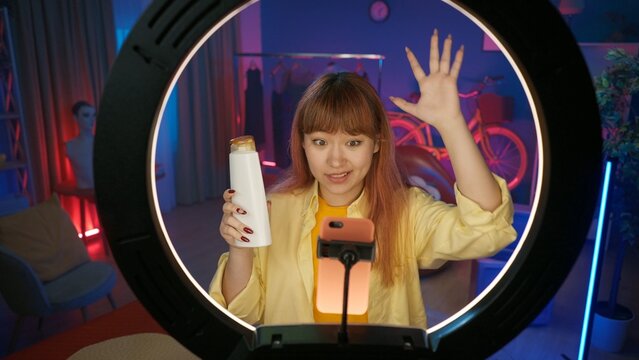 Beautiful girl beauty vlogger advertises a hair shampoo in front of the camera at home studio.